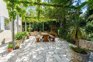 A stone patio with a wooden table and chairs, surrounded by potted plants and a pergola. - Apartments &amp; Rooms Jokovic-standard Double Room With Terrace and Partial Sea View (Zupa dubrovacka)