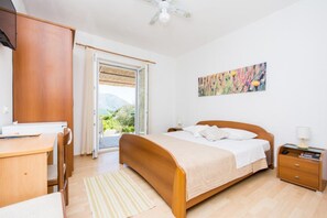 A bedroom with a bed, a desk, a chair, a nightstand, a lamp, and a painting on the wall. - Apartments &amp; Rooms Jokovic-standard Double Room With Terrace and Partial Sea View (Zupa dubrovacka)