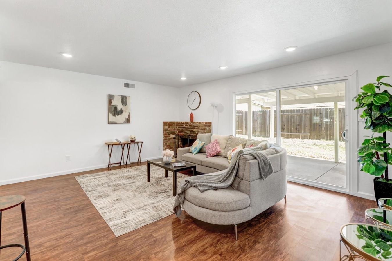 A spacious living room with hardwood flooring, a grey sofa, a coffee table, and a large window with a view of a backyard.