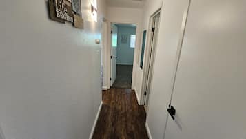 A hallway with white walls, wooden flooring, and a door leading to another room.