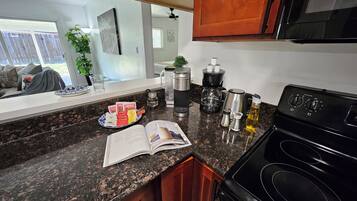 A kitchen with granite countertops, a black stove, and various appliances including a coffee maker and a kettle.