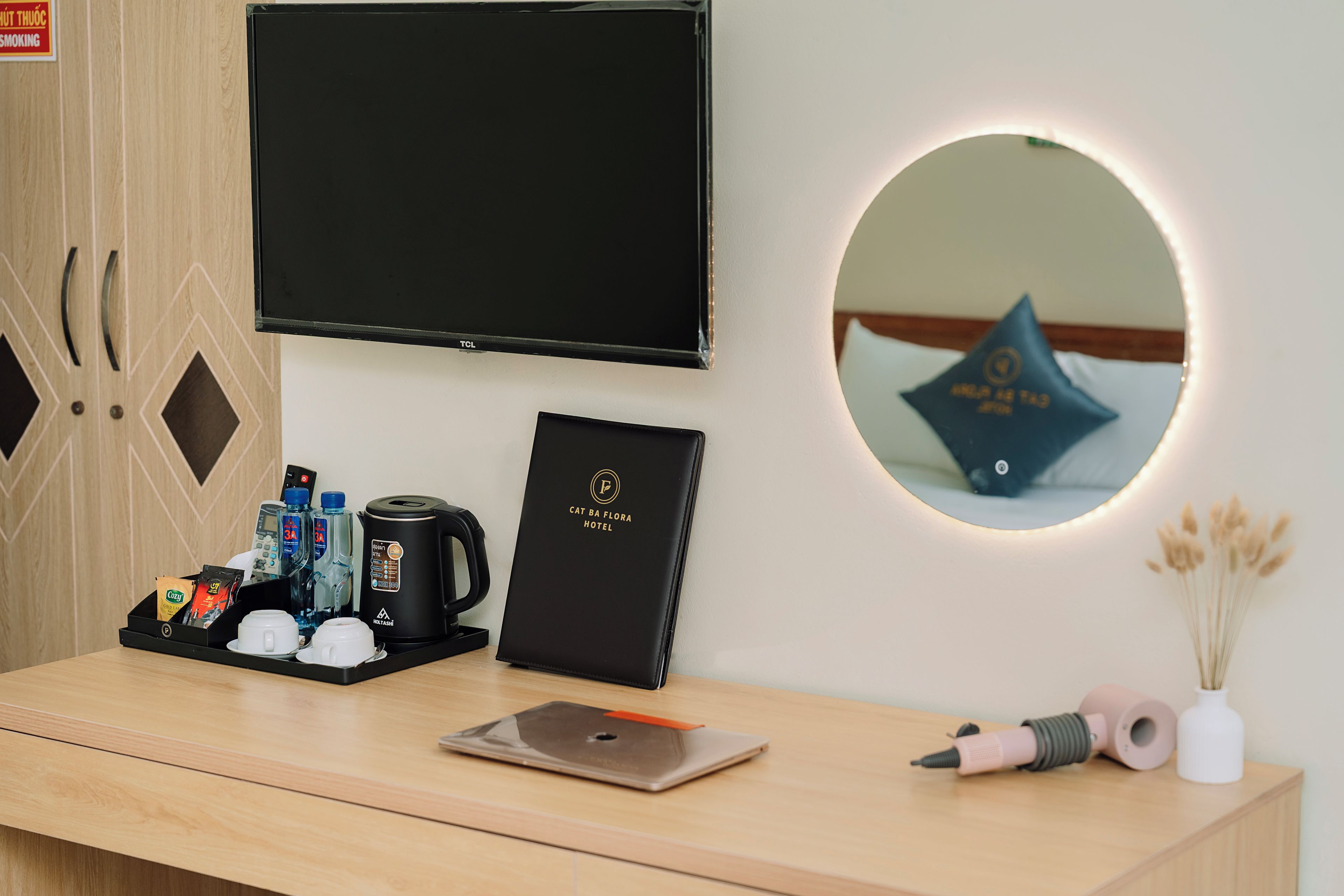 Una recepción de hotel con un televisor de pantalla plana, un certificado enmarcado, una cafetera, un hervidor de agua, un dispensador de agua y un teléfono inteligente.
