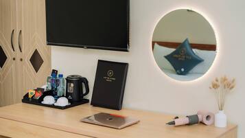 Una recepción de hotel con un televisor de pantalla plana, un certificado enmarcado, una cafetera, un hervidor de agua, un dispensador de agua y un teléfono inteligente.