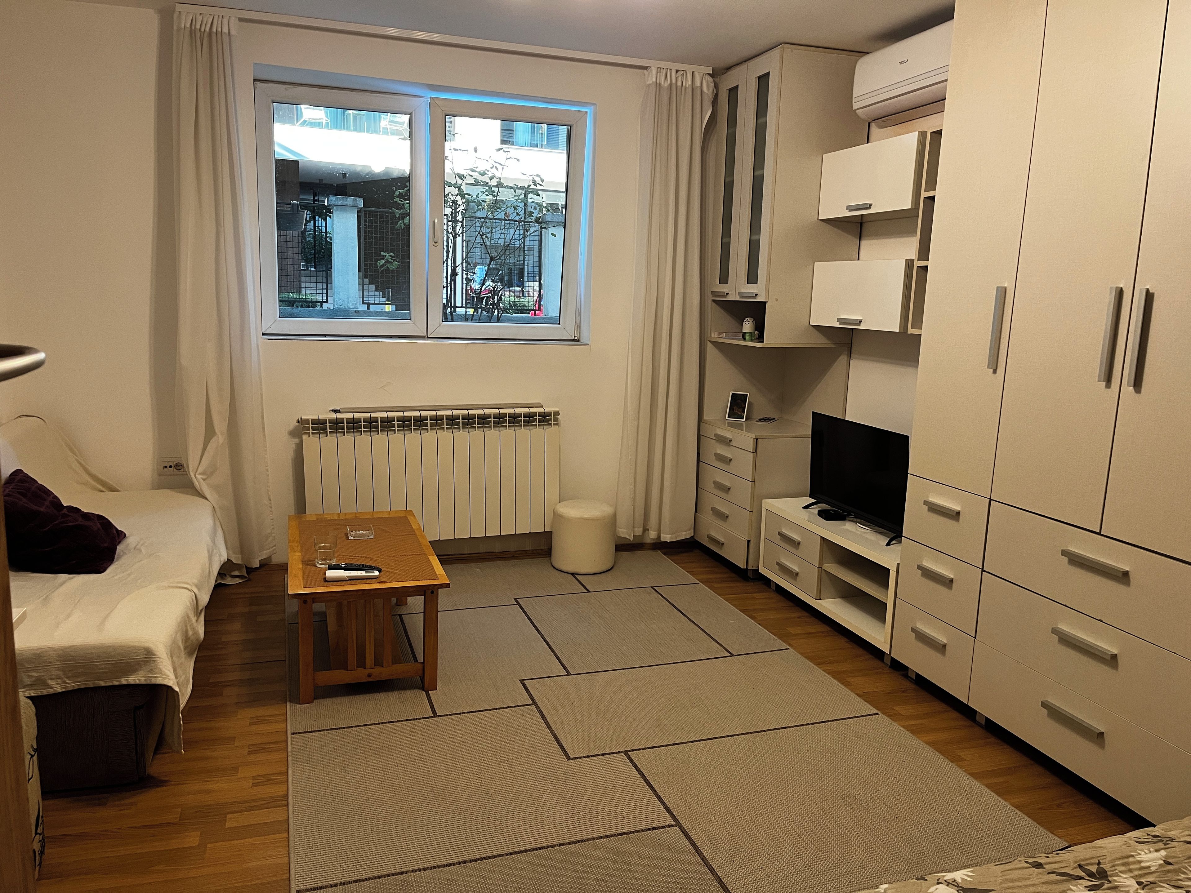 A compact room with a bed, a small table, a television, and a wardrobe.