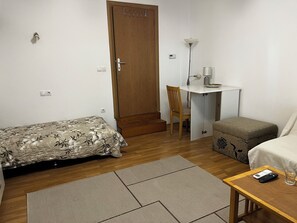 A small, furnished room with a bed, a desk, a chair, a sofa, and a small table with a remote control and glass. - Perfect 1-bedroom apartment with AC in fabulous Beograd (Beograd)