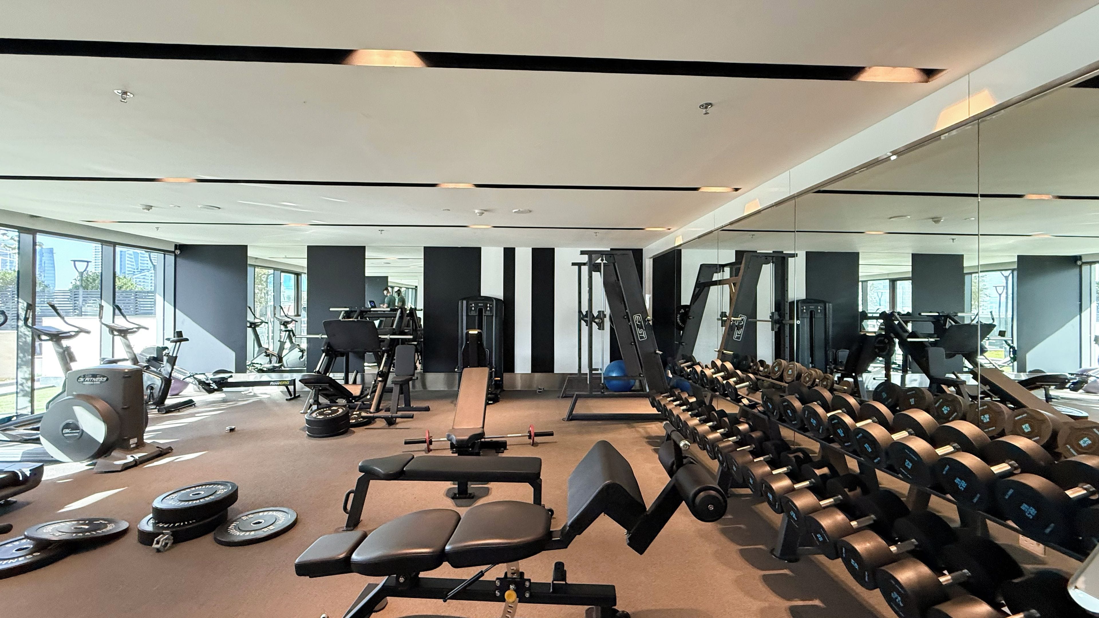 Uma academia com diversos equipamentos de exercício, incluindo esteiras, aparelhos de musculação e pesos livres.