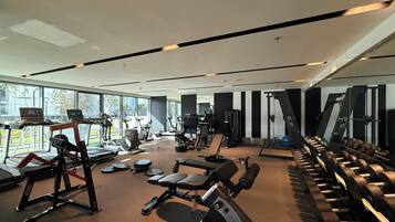 Un gimnasio moderno con máquinas de cardio, equipo de levantamiento de pesas y un amplio muro de espejos.