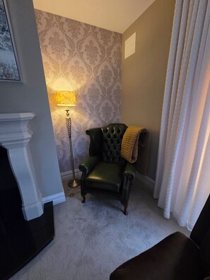 A room with a patterned wallpaper, a green leather armchair, a floor lamp, and a white fireplace. - Superb 4-bedroom house in WH perfect for family getaways (WH)