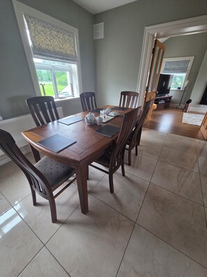 A dining area with a wooden table, chairs, and a view of the outdoors through a window. - Superb 4-bedroom house in WH perfect for family getaways (WH)