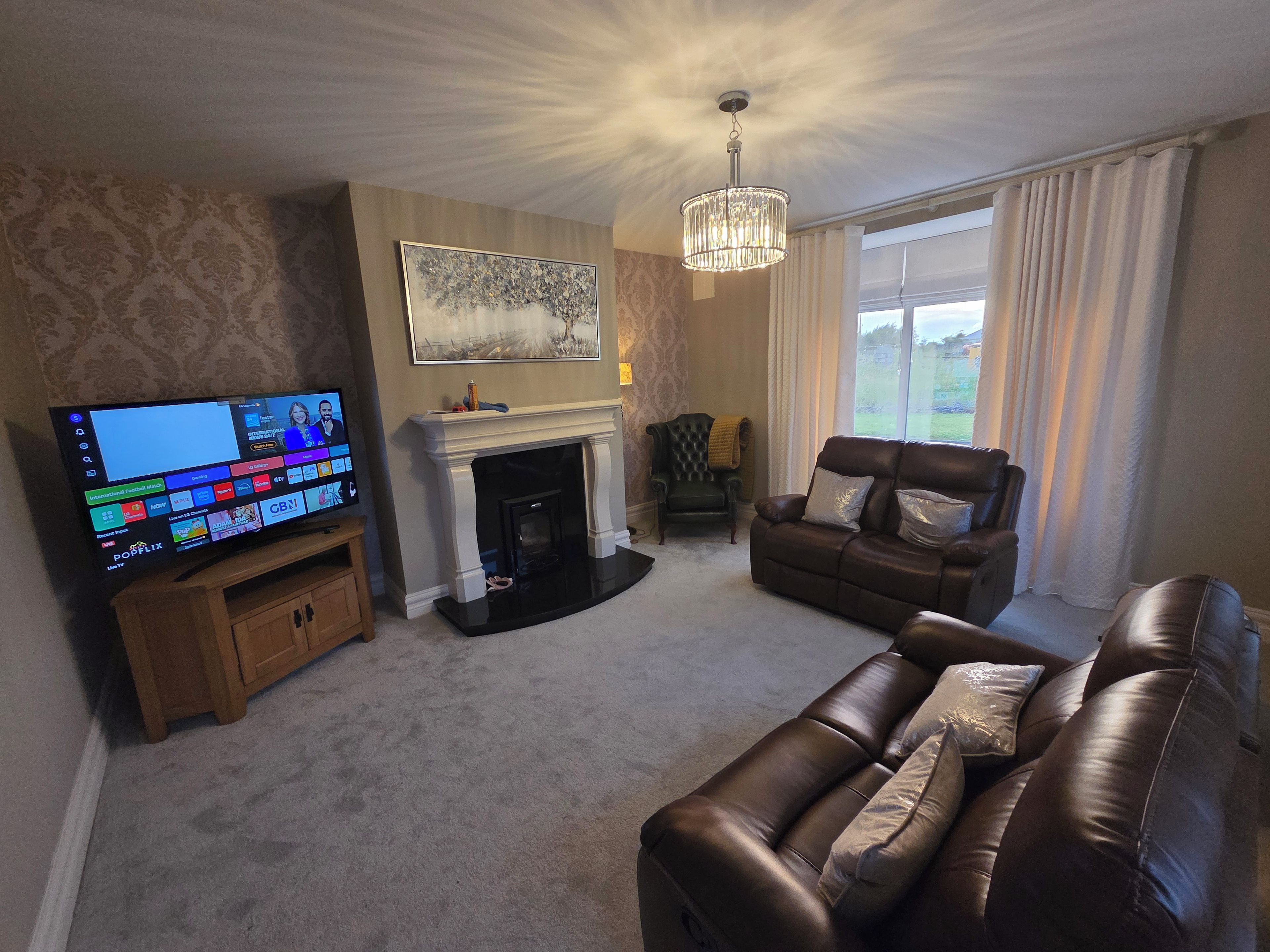A living room with a fireplace, a leather sofa, a television, and a chandelier.