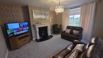 A living room with a fireplace, a leather sofa, a television, and a chandelier.