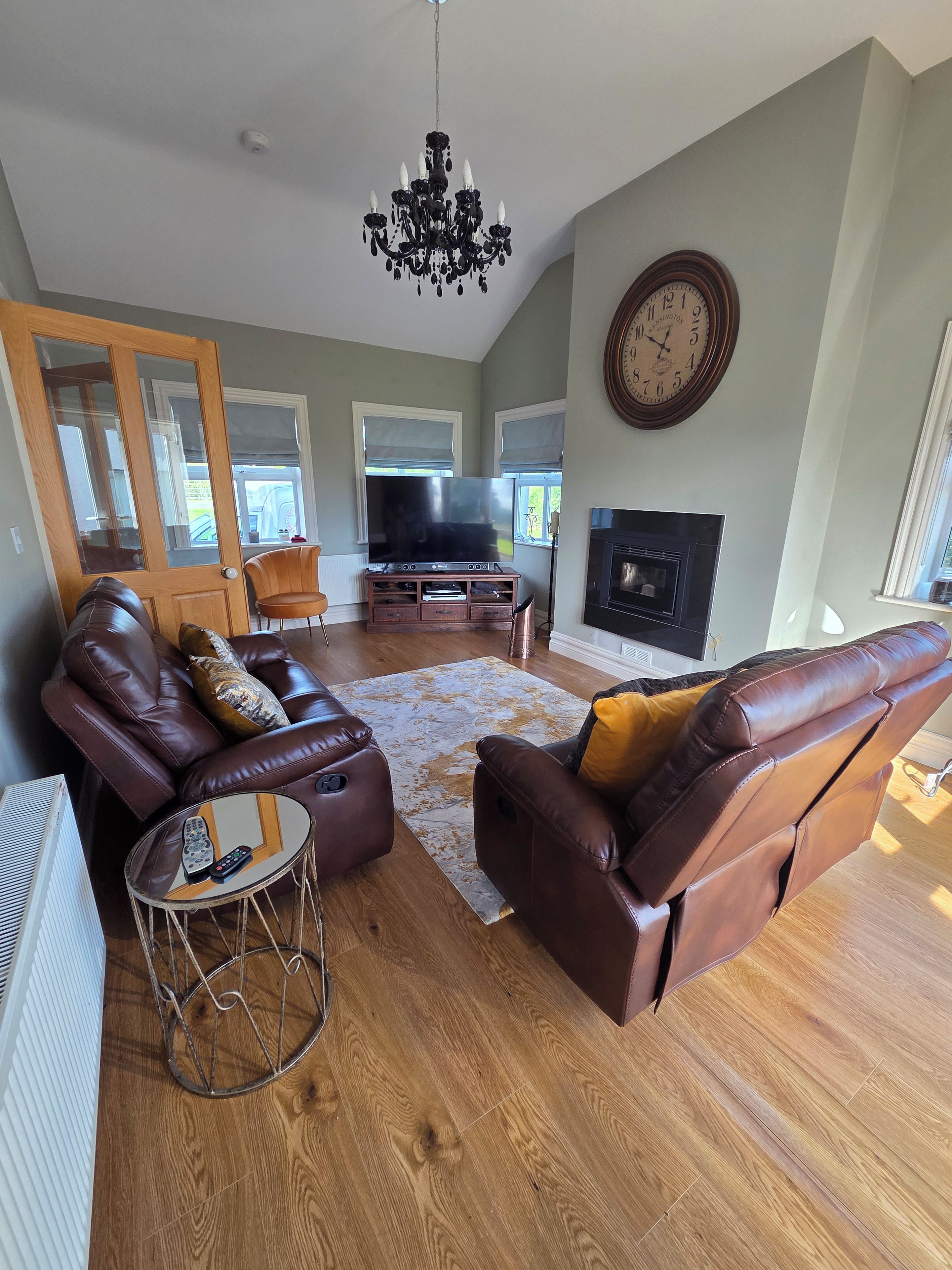 A living room with a leather sofa, a television, a fireplace, and a chandelier.