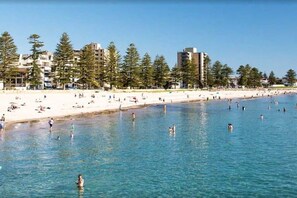 A beach with clear water, people swimming, and buildings in the background.