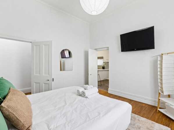 A hotel room with a bed, a flat-screen TV mounted on the wall, and a door leading to a bathroom.