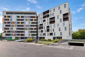 A modern multi-story residential building with balconies, a parking area, and a clear sky. - Cracow | Poznańska 10 | Comfortable Apartment | Air conditioning (Kraków)