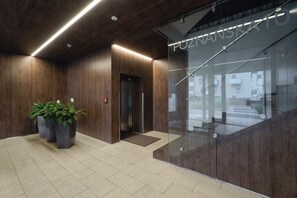 A modern interior with a wooden wall, a glass elevator, and potted plants. - Cracow | Poznańska 10 | Comfortable Apartment | Air conditioning (Kraków)
