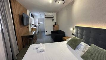 Habitación de hotel con cama, escritorio, silla, televisor y una pequeña zona de estar.