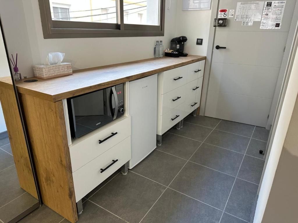 Una cocina compacta con microondas integrado, cafetera y un refrigerador pequeño.