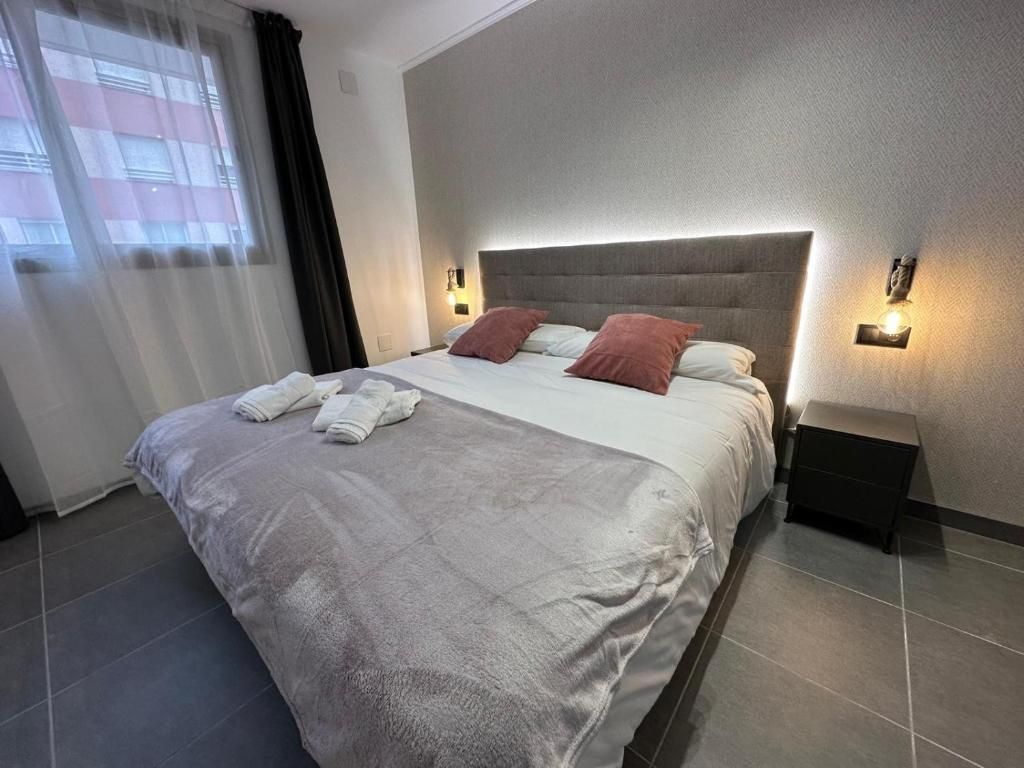 Una cama bien hecha con almohadas y toallas, una mesita de noche con lámpara, y una ventana con cortinas.