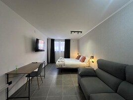 Una habitación de hotel moderna con cama, sofá, escritorio y televisión.