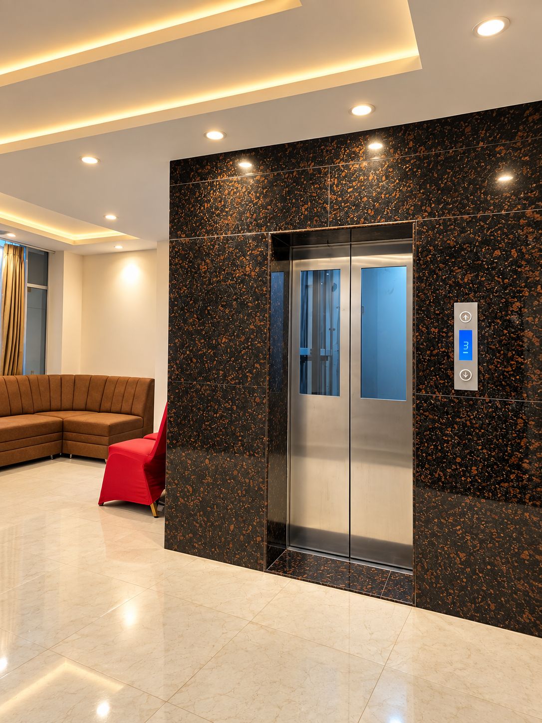 A modern elevator with a digital display, a red chair, and a brown sectional sofa in a lobby with a speckled black and gold wall.