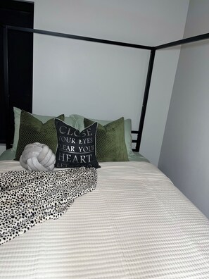 En seng med en sort pude med hvid tekst, et leopardmønstret tæppe og grønne puder.