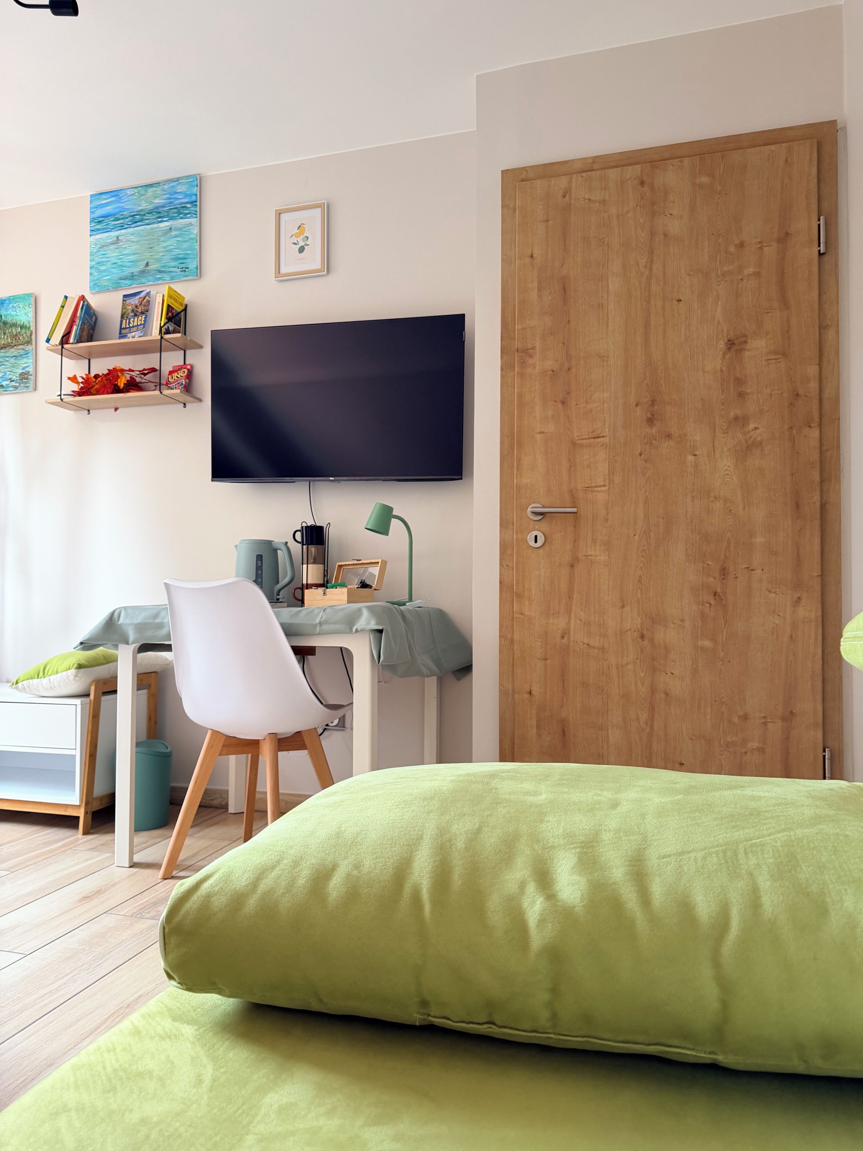 Ein Zimmer mit einem Bett, einem Schreibtisch, einem Stuhl, einem Fernseher und einer Holztür.