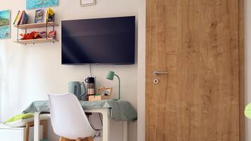 Ein Zimmer mit einem Bett, einem Schreibtisch, einem Stuhl, einem Fernseher und einer Holztür.
