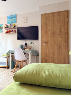 A room with a bed, a desk, a chair, a television, and a wooden door.