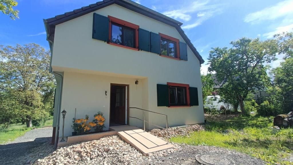 Una casa de dos pisos con entrada principal, un porche pequeño y un jardín con flores y un camino.