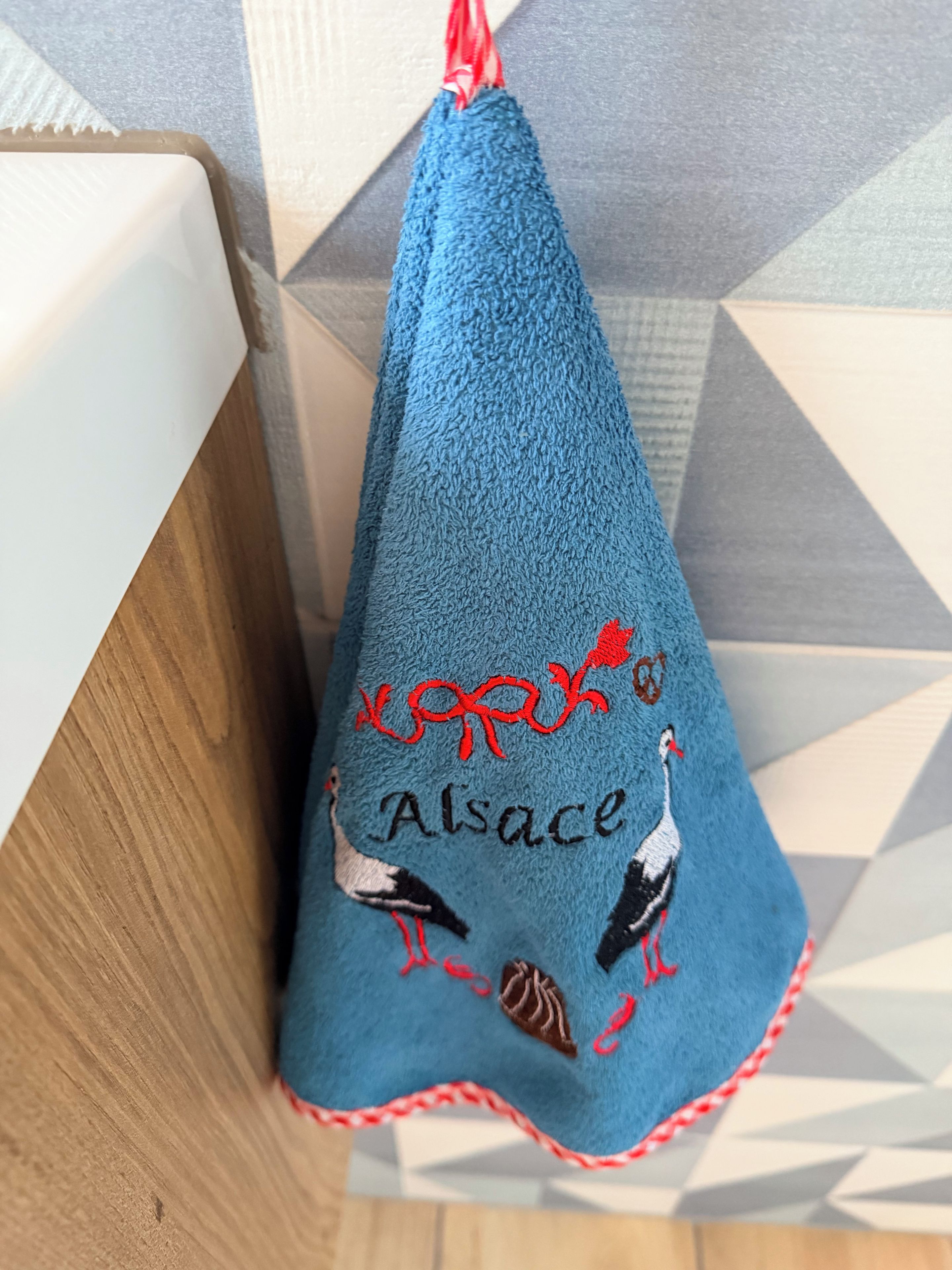 A blue towel with embroidered birds and text, hanging on a wooden surface.