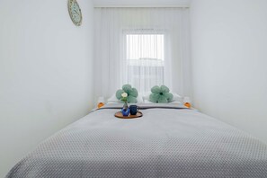 A neatly made bed with a grey textured bedspread, a small vase with a single flower, and two green decorative pillows. - Kolobrzeg | Bałtycka 11B | Cosy Apartment | Private garden (Kołobrzeg)