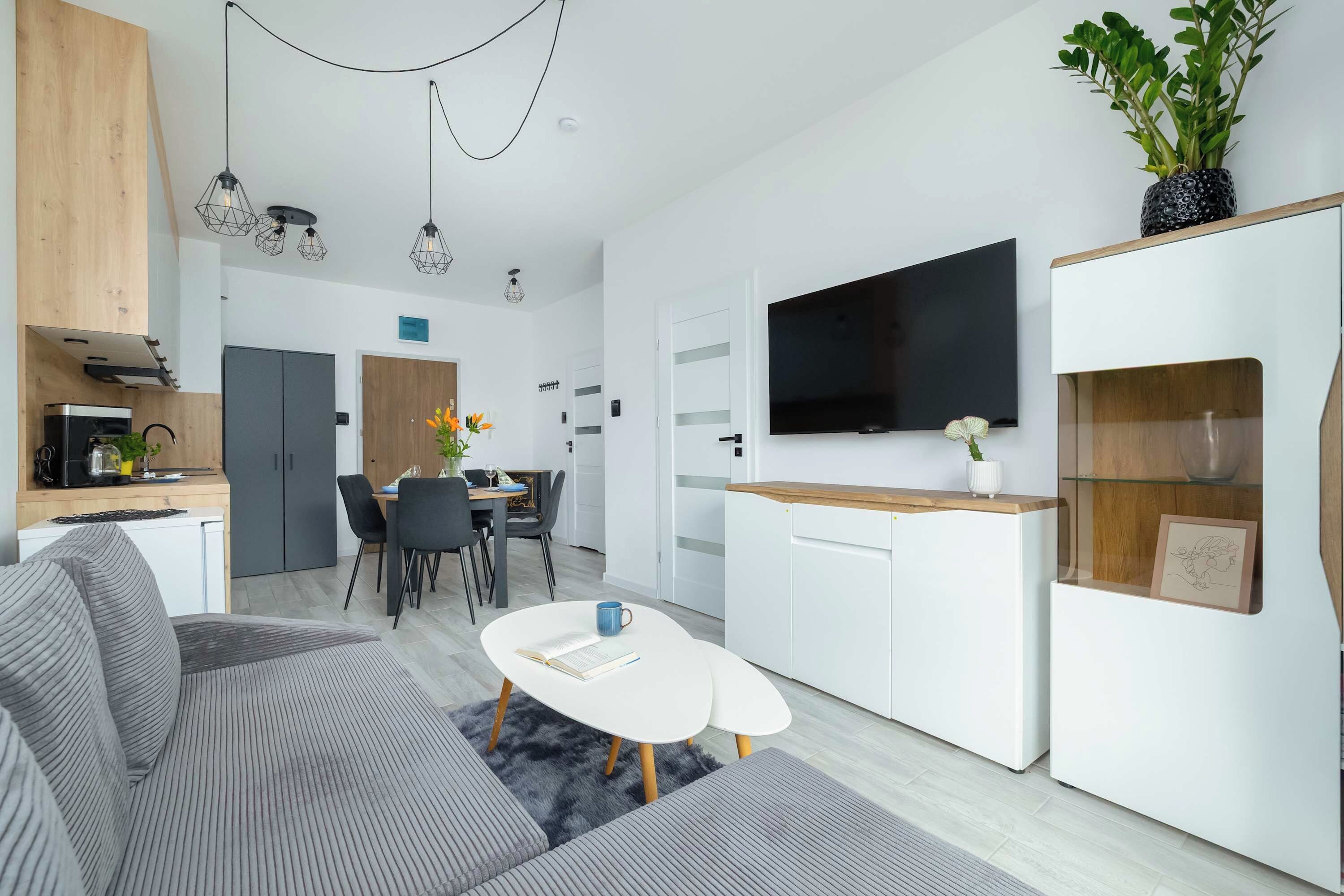 Une cuisine moderne avec un coin repas, un téléviseur à écran plat fixé au mur et un coin salon confortable avec une table basse.
