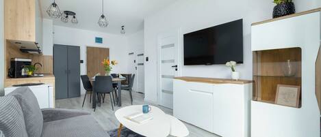 A modern kitchen with a dining area, a flat-screen TV mounted on the wall, and a cozy seating area with a coffee table.