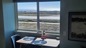 A room with a table and chairs, a window with a view of the beach, and a framed picture on the wall.