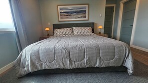 A bed with a striped bedspread, two bedside lamps, a framed picture on the wall, and a door in the background. - Point Arena Lighthouse - Driftwood Suite (Point Arena)