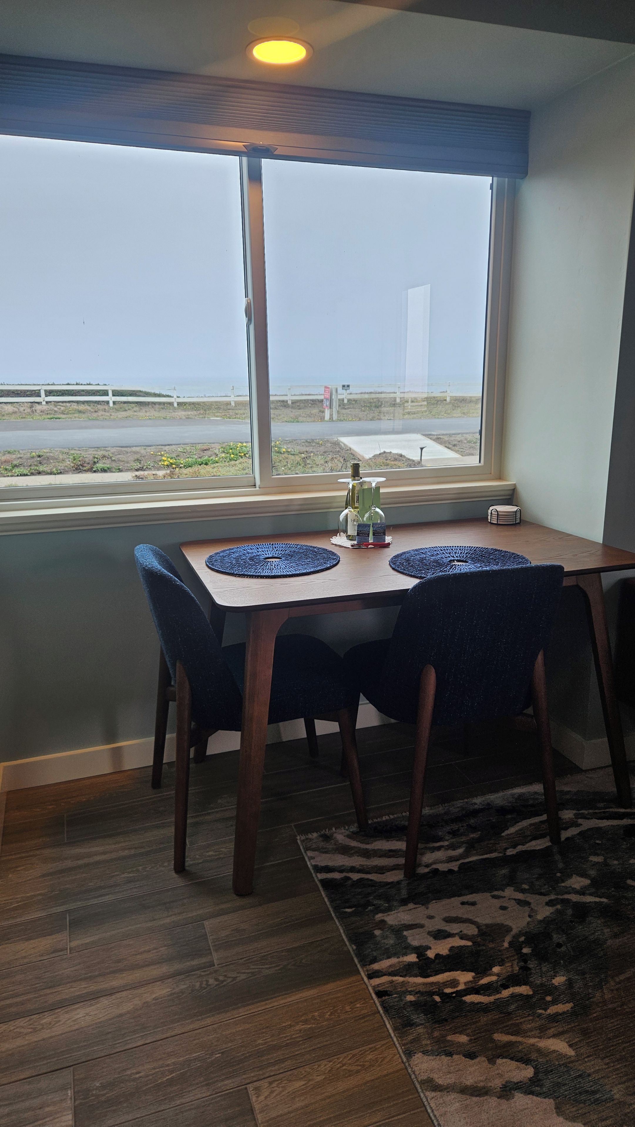 A dining area with a table and chairs, a view of the beach, and a window with blinds.