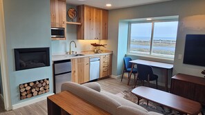 A compact kitchen with a microwave, sink, and wooden cabinets. There's a dining area with a table and chairs, a sofa, and a fireplace. - Point Arena Lighthouse - Driftwood Suite (Point Arena)
