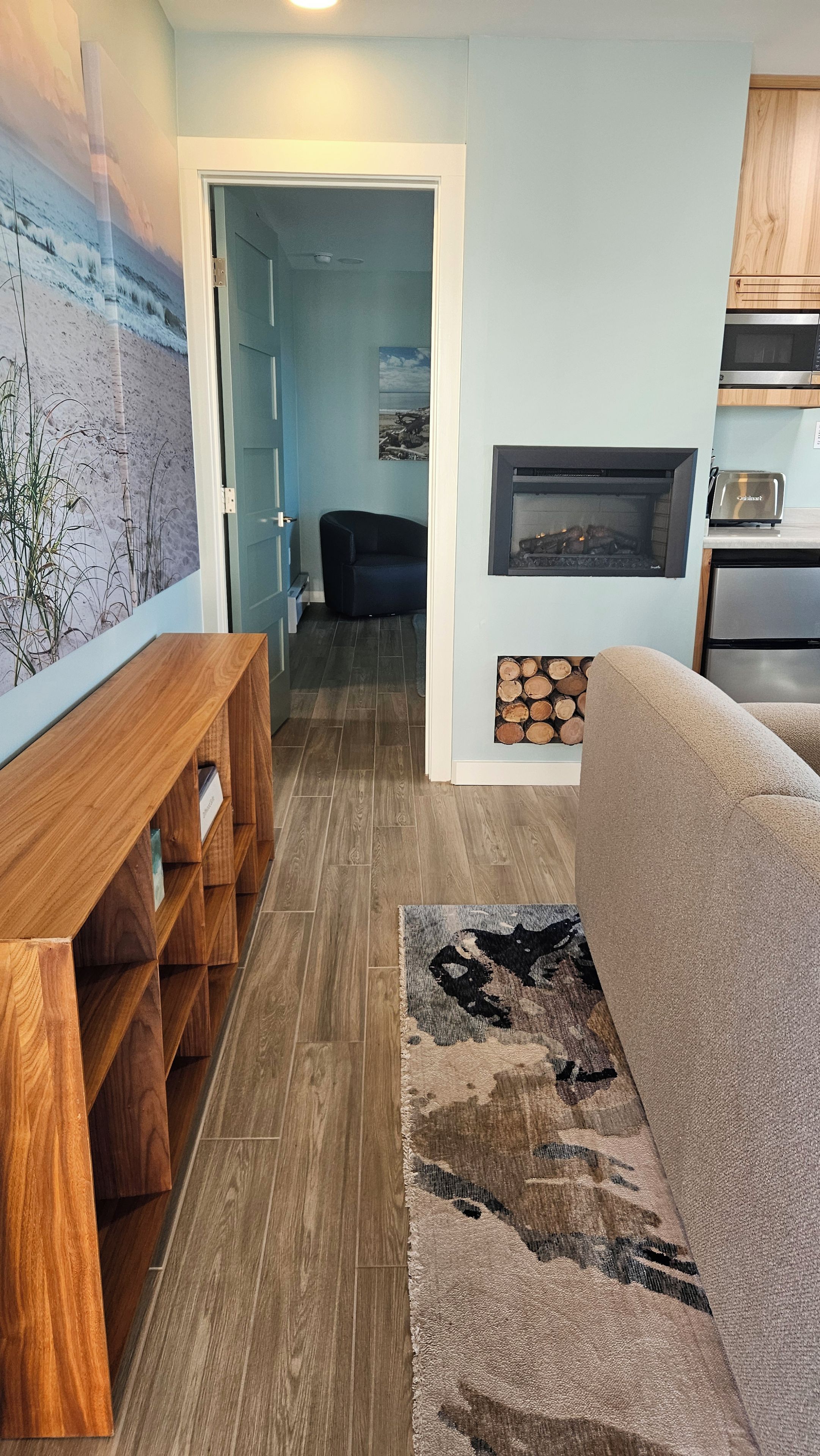 Een moderne woonkamer met een houten bank, een open haard en een keuken die door een open deur zichtbaar is.