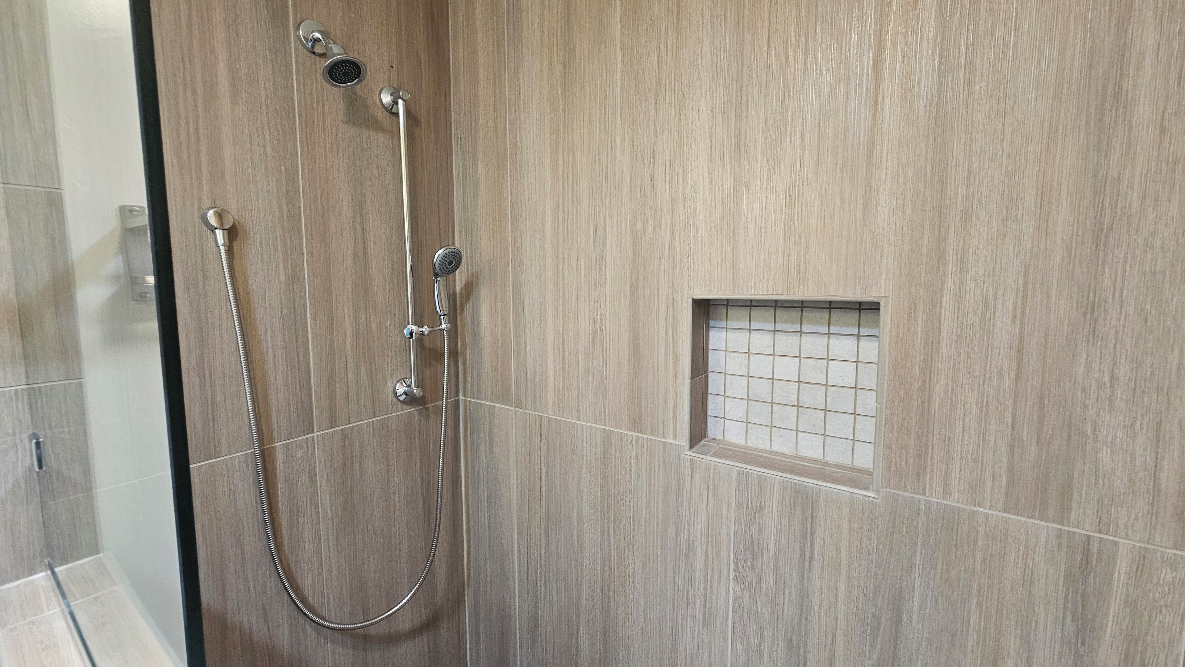 A shower with a handheld showerhead, a wall-mounted showerhead, and a handheld shower hose.