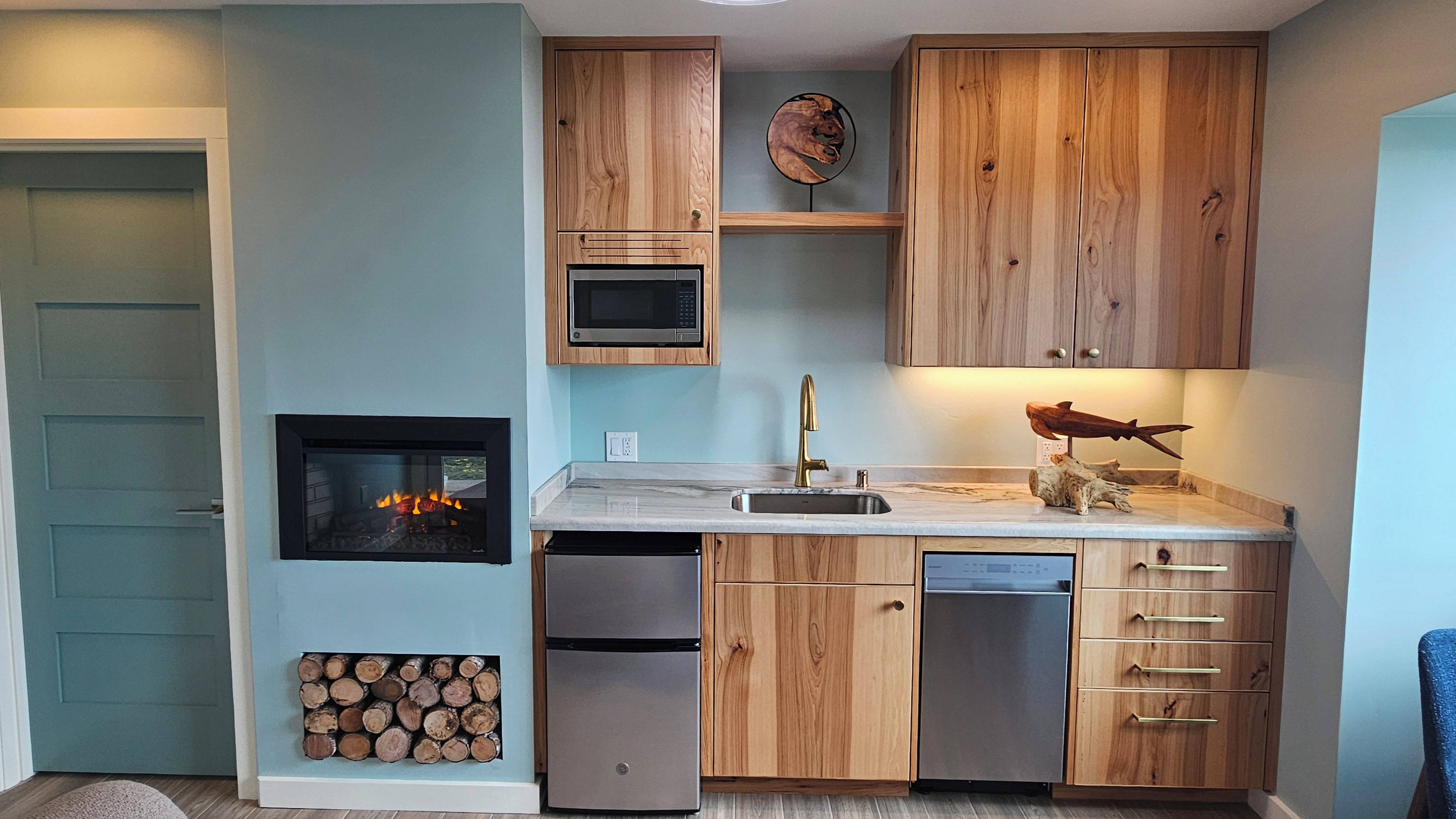 Une cuisine compacte avec des meubles en bois, un four à micro-ondes encastré, un réfrigérateur en acier inoxydable et un poêle à bois.