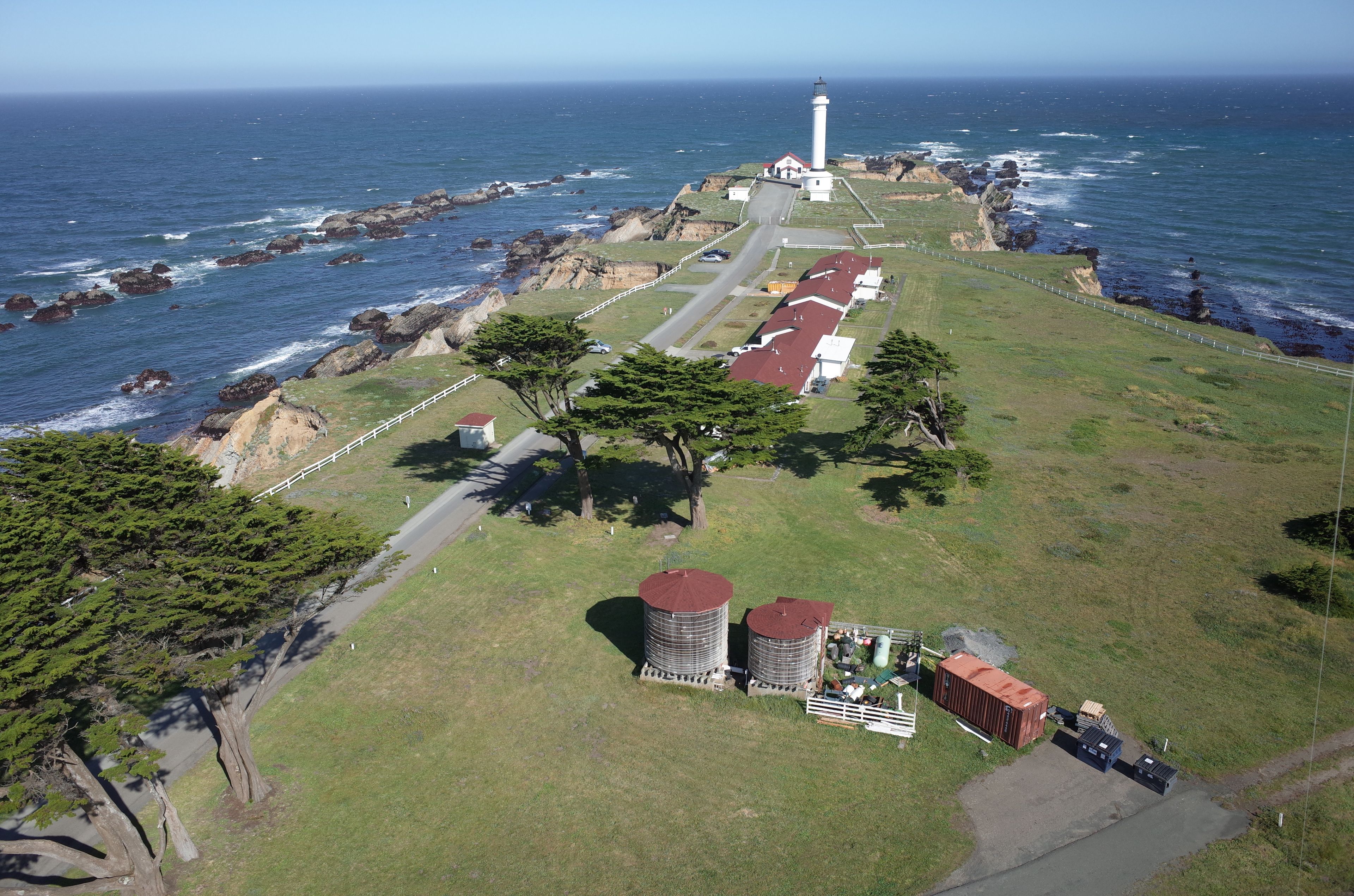 A coastal property with a lighthouse, a paved road, and a grassy area with trees.