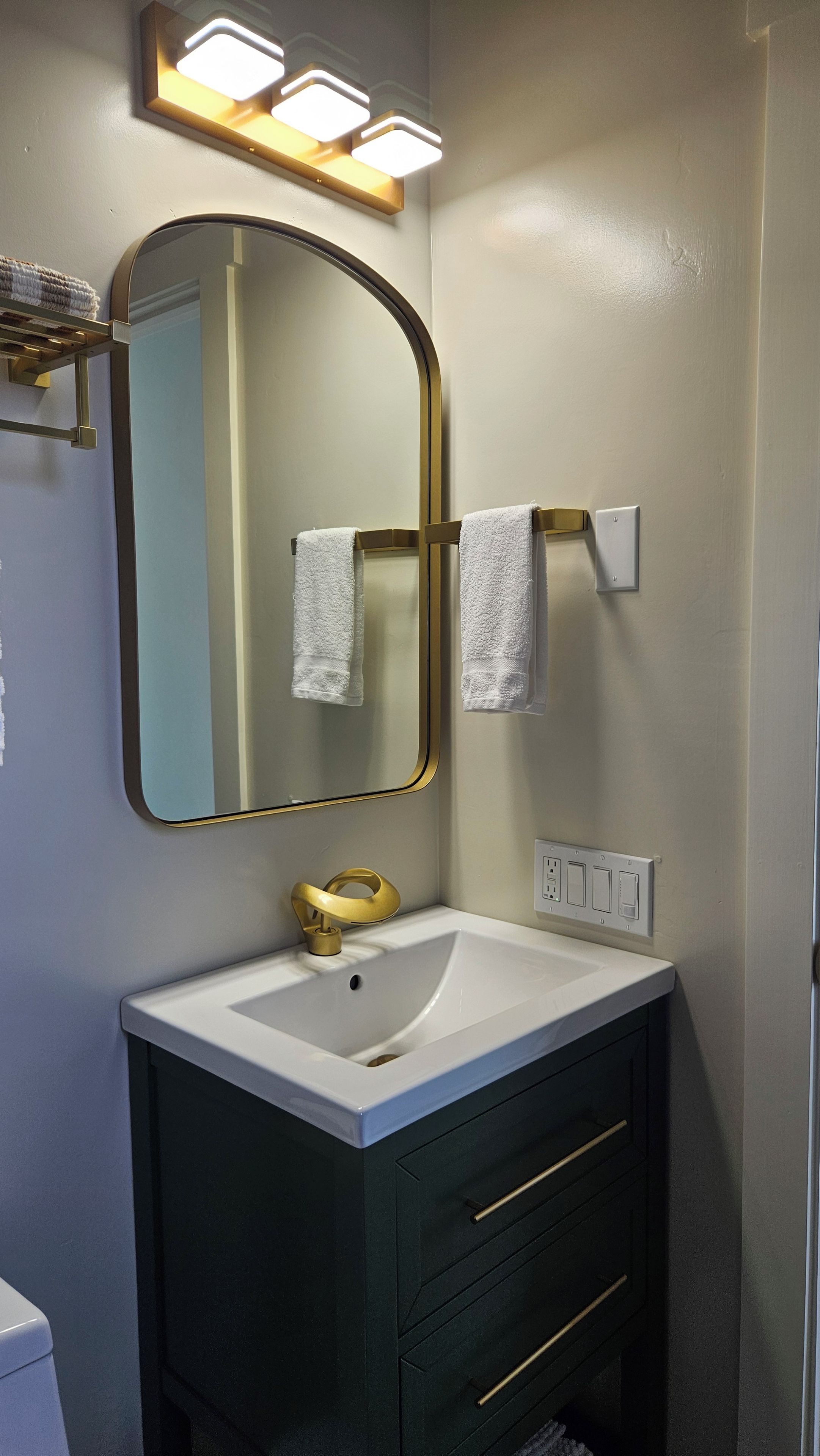 Een badkamer met een witte wastafel, een spiegel met gouden lijst en een handdoekrek.