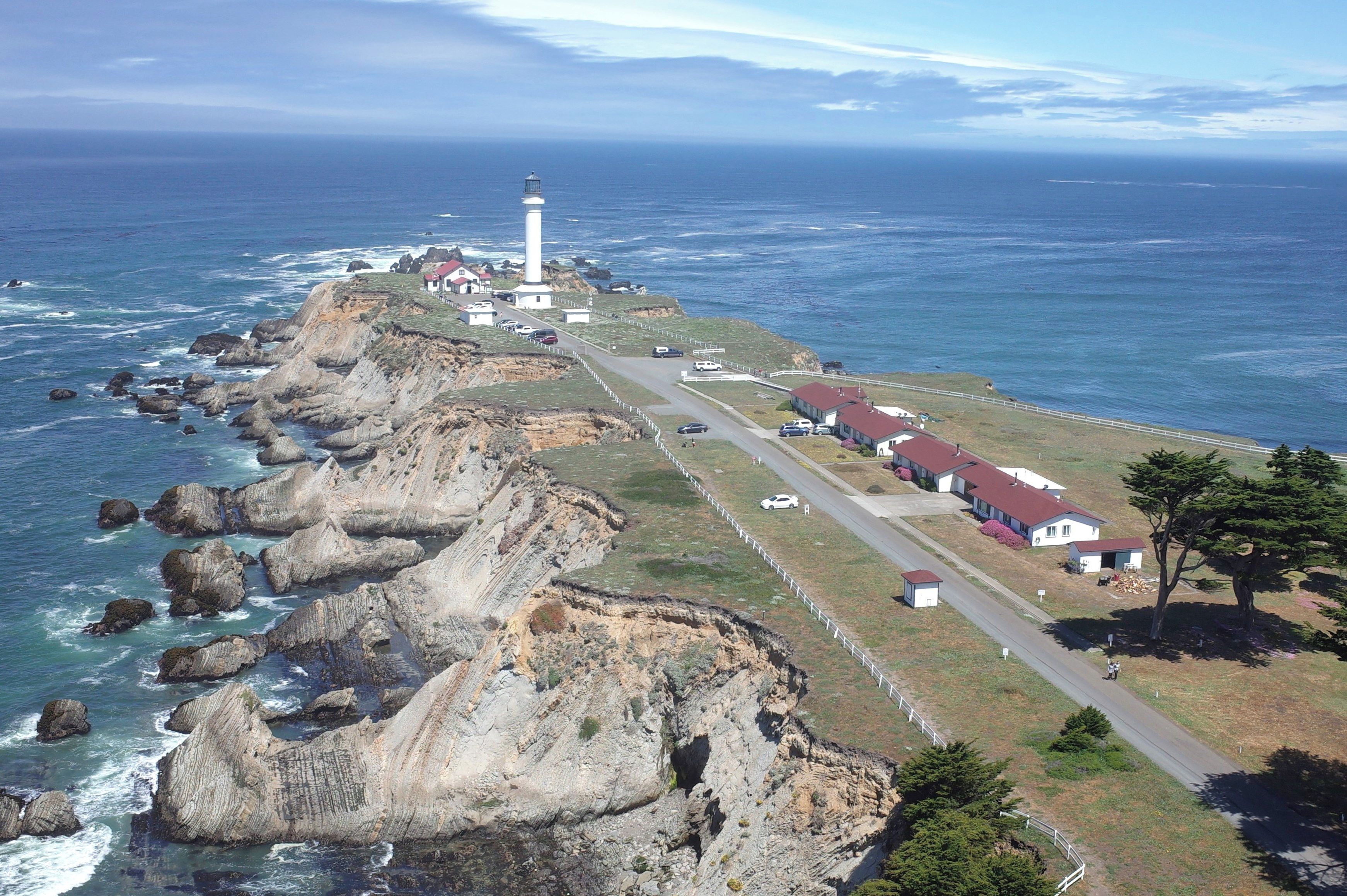 A coastal property with a lighthouse, rocky cliffs, and a road leading to a row of houses.