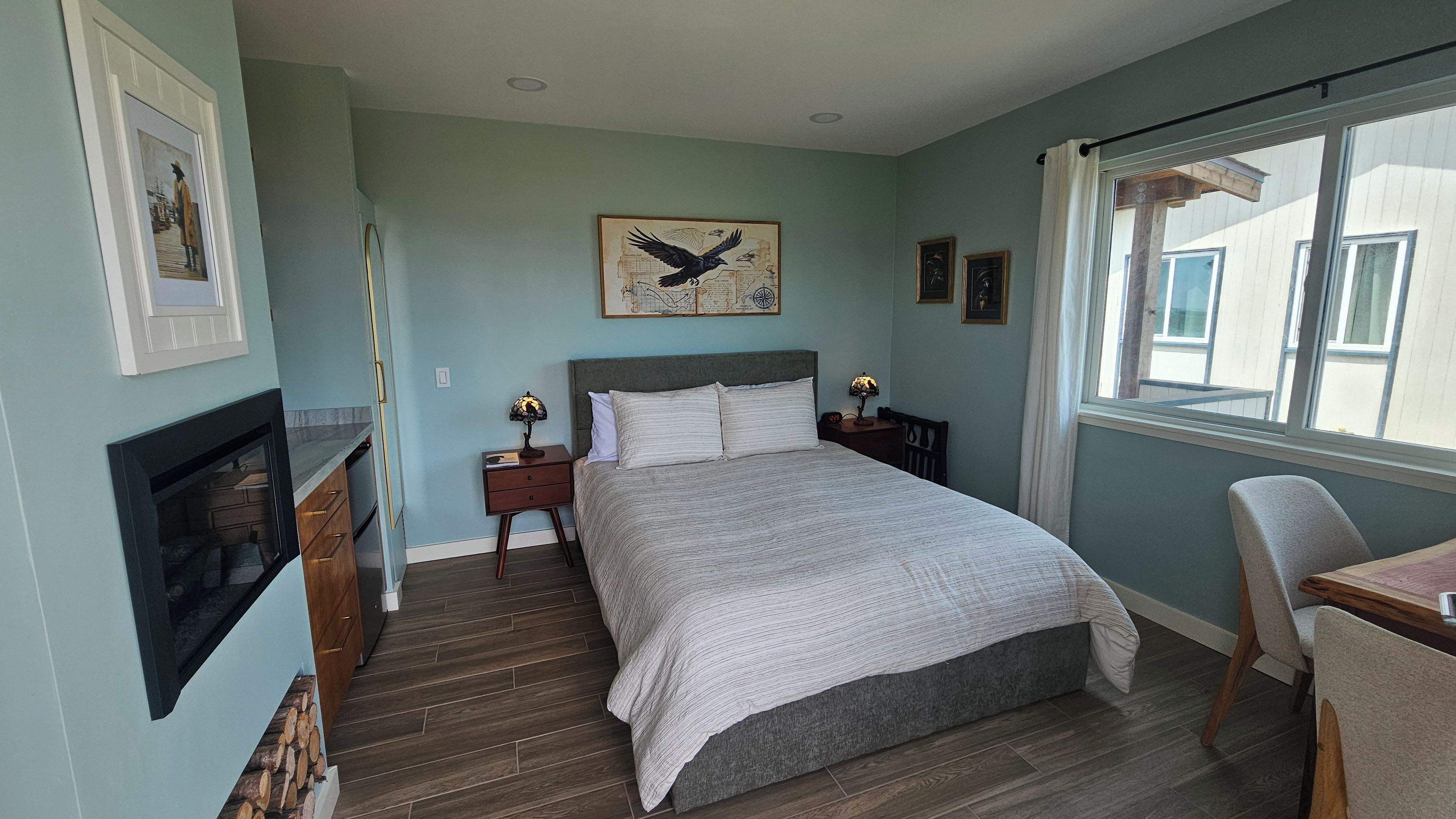 A bedroom with a bed, bedside tables, a nightstand, a chair, a window, and a fireplace.