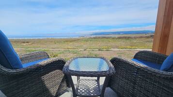 Wicker chairs with cushions and a glass table in an outdoor setting with a view of the ocean.