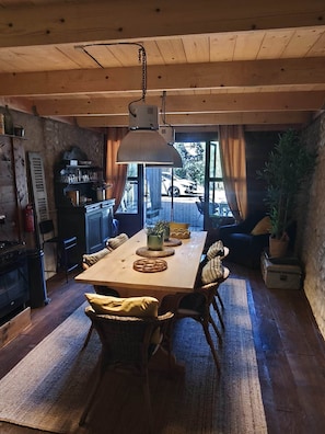 Een eetruimte met een houten tafel, stoelen, een hanglamp en uitzicht op buiten.