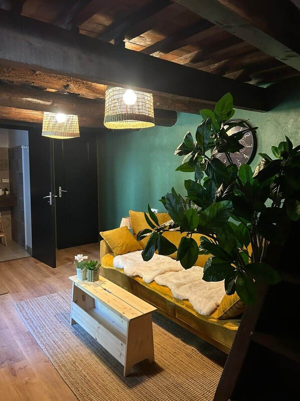 Een gezellige kamer met een bank, een houten salontafel, een grote plant en een wandklok.