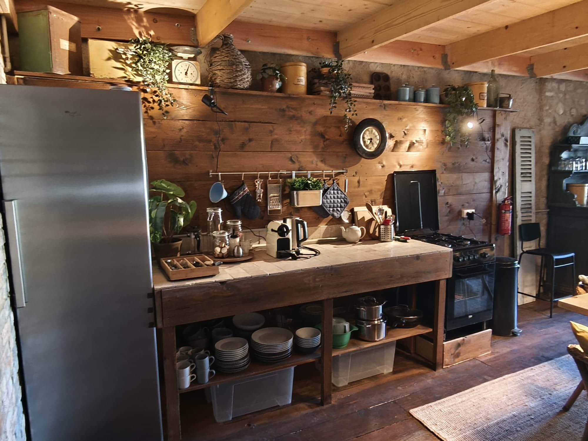 Une cuisine rustique aux murs en bois, dotée d’un réfrigérateur en acier inoxydable et d’une variété d’ustensiles et d’appareils de cuisine.