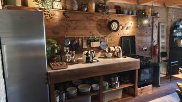 Une cuisine rustique aux murs en bois, dotée d’un réfrigérateur en acier inoxydable et d’une variété d’ustensiles et d’appareils de cuisine.